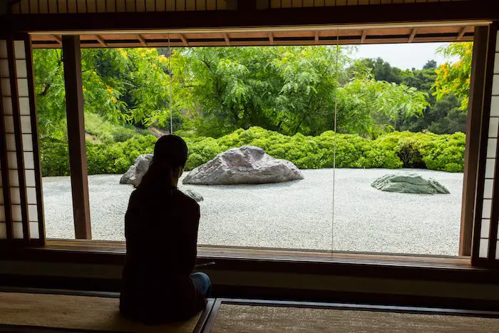 Woman looking through a window at a Japanese Zen Rock Garden.