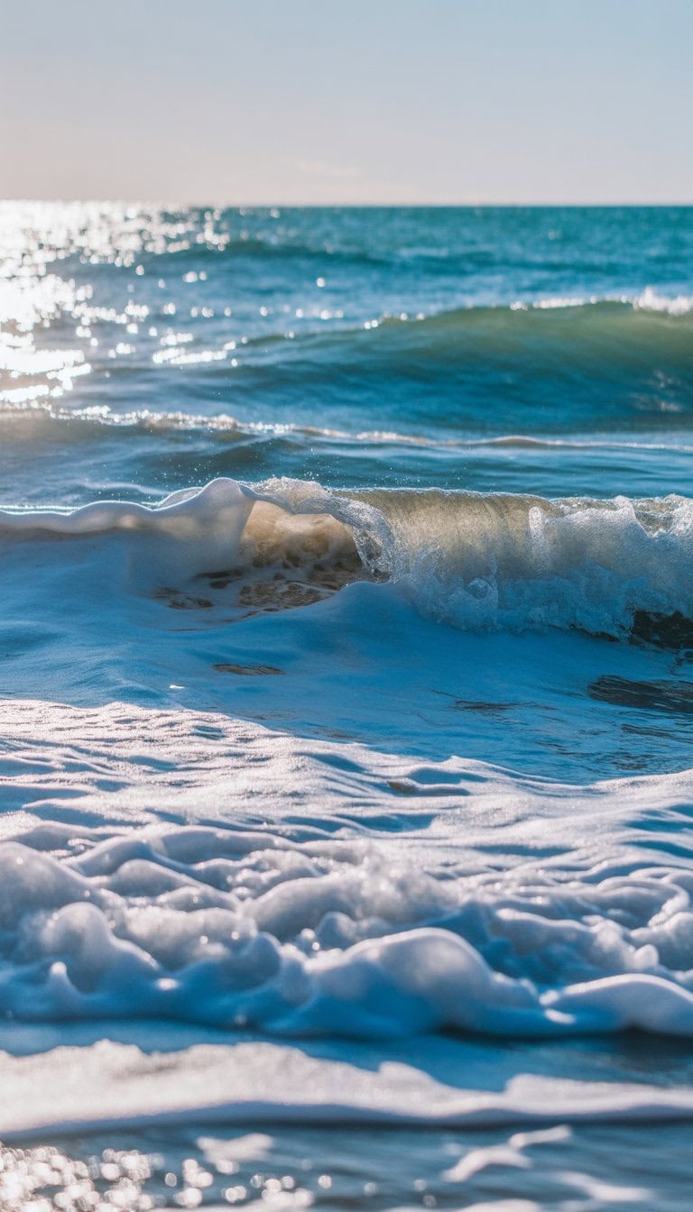 Ocean waves with blue water and white foam rolling onto a sandy shore under a clear sky.